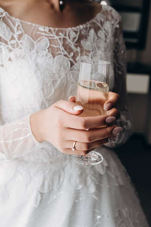 Vertical image of bride hand with perfect design manicure holding glass of fresh champagne. Bride morning. Female beauty and elegance.の写真素材