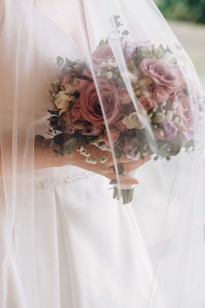 Bride's hands holding modern a beautiful, stylish wedding bouquet of purple, pink roses and...
