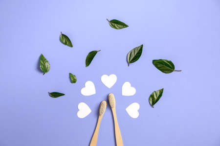 Two wooden bamboo eco friendly toothbrushes, green leaf, white heart on purple background. Dental care, eco friendly, reuse and valentines day concept. Flat lay, top view, copy spaceの写真素材