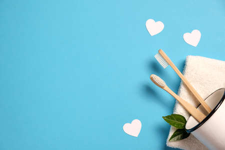 Zero waste concept. Two wooden bamboo eco friendly toothbrushes in metal cup, green leaf, white hearts and towel on blue background. Eco friendly, valentines day concept. Flat lay, copy spaceの写真素材