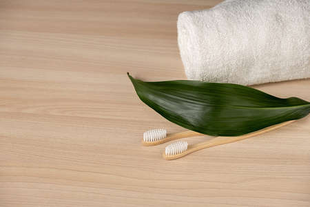 Natural bamboo toothbrush, white towel on wooden background with green leaf. Zero waste concept. Plastic free essentials, teeth care. Sustainable lifestyleの写真素材