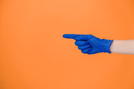 Close up of male finger pointing at copy space, wears medical protective latex gloves, isolated on orange studio background with copy space for advertisement. Advertising area, mockup. Hand gestureの写真素材