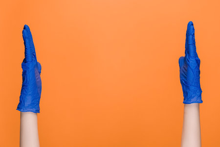 Male hands in medical protective latex gloves showing big size gesture, demonstrate something wide, isolated on orange studio background with copy space for advertisement. Body language conceptの写真素材