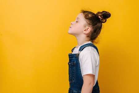 Profile side view of happy sweet little preschool girl do deep breath enjoy fresh air or dreaming fill with energy feeling healthy good concept, models over yellow studio background with copy spaceの写真素材