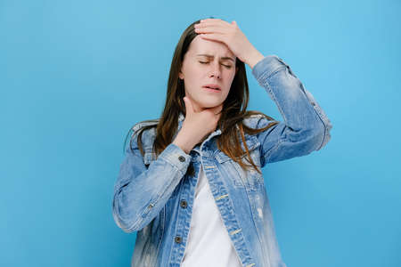 Disappointed millennial young female covers face with his hand, unhappy brunette woman feeling hopeless, suffering from stress and nervous tension, posing isolated on blue studio background wallの写真素材