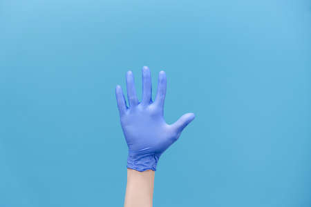 Numbers calculating. Close up of unrecognizable young man counting from 5 with fingers, wears medical protectives gloves, isolated on blue background with copy space for advertisement. Hand gestureの写真素材