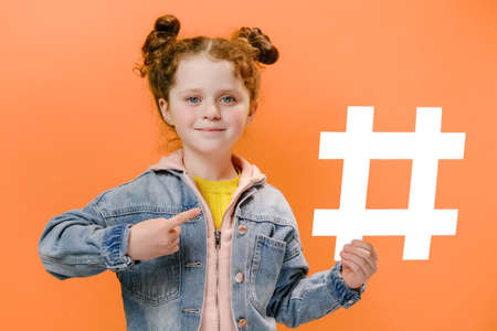 Attractive preschooler girl child pointing hashtag symbol, famous children blog, posing isolated...