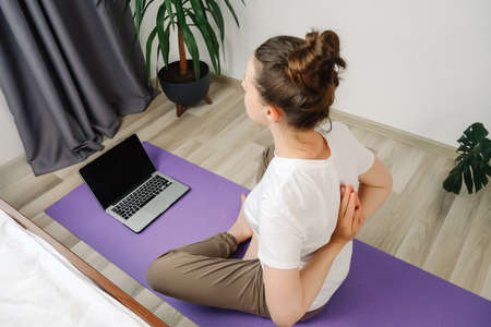 Healthy young female meditating at home watching online tv yoga class e tutorial on laptop doing...