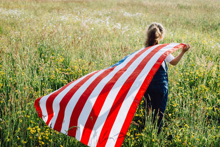 Close up back view of little playful preschool girl run across green field with national USA flag...