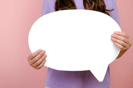 Close up of unrecognizable young caucasian female demonstrate white blank speech bubble with copy space for promotional content, isolated over pink studio background wall. Advertising area mock upの写真素材