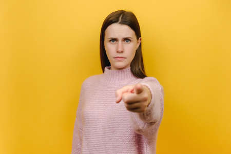 Portrait serious strict attractive young caucasian woman 20s wearing pink knitted sweater point index finger camera on you motivating commanding do it, isolated on yellow color background studioの写真素材