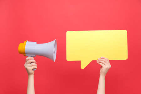 Close up of female hands holding an empty yellow paper speech bubble and megaphone, isolated over pastel red background studio with copy space for your text or design. Social media marketing conceptの写真素材