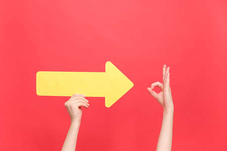 Female hands holding yellow arrow points to Okay gesture, demonstrates approval or agreement,...