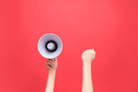 Close up of female hands holding megaphone and raised fist, political protest to showing his power, isolated on red studio background with copy space for your text or design. Concept revolution, fightの写真素材
