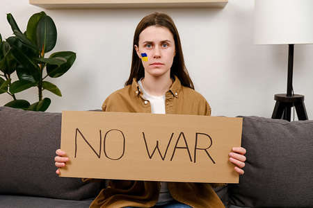 Young woman with flag of Ukraine on face protesting war conflict raises banner with inscription message text No War. Crisis, peace, stop aggression, Russian war invasion. Stop War in Ukraine. Prayの写真素材
