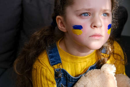 Portrait of upset sad little girl child with flags of ukraine on face. Peace, no war, help, stop russian aggression. Freedom to Ukraine, Crisis concept. hope for the world. Anxiety and anticipationの写真素材