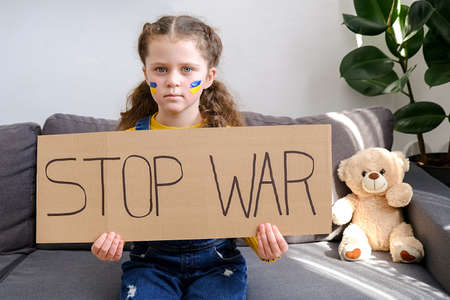 Upset Ukrainian little girl protesting war conflict holding banner with inscription message text...