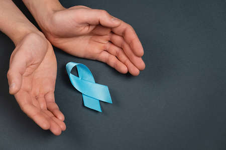 Close up of male hands and blue ribbon on gray studio background wall. Prostate Cancer Awareness, Movember Men's health awareness. Healthcare, International men, Father and World cancer day conceptの写真素材