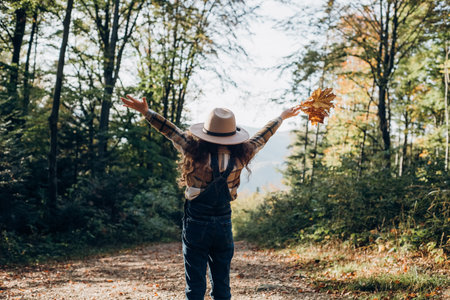 Back view of funny little girl kid in hat against autumn forest and amazing mountains at sunny day....