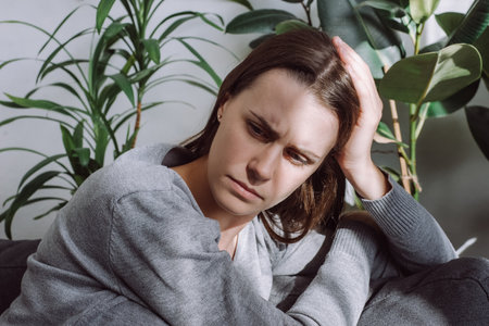 Close up of desperate girl in trouble having problem, regret mistake abortion, alone at home. Upset depressed young woman 20s feeling tired bad down headache migraine sitting on sofa in living roomの写真素材