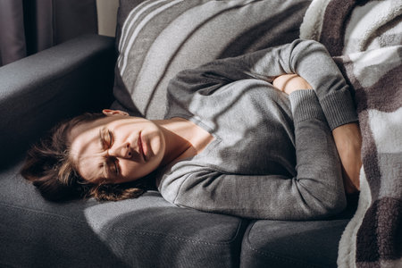 Depressed young caucasian woman lying sofa with her arms around herself, unhappy caucasian female brunette suffering from insomnia depression, psychological problem, concept impotence, astheniaの写真素材