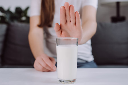 Selective focus of female hand in deny, no or push out to avoid for drink milk, girl sit on couch at home, bad stomach ache. Lactose intolerance and dairy food, health problem, belly suffer conceptの写真素材