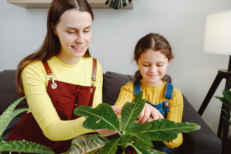 Smiling young mother and daughter cleans indoor plants, takes care green leaf. Gardening, housewife and housework chores concept. Home hobbies, growing plants, gardener or florist work small shopの写真素材