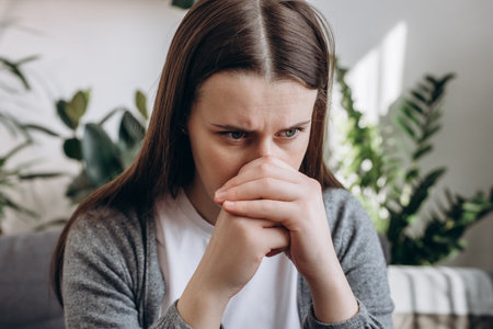 Close up of stressful sad young caucasian woman sitting alone on couch in living room covering face with hands. Emotional brunette female 20s feeling upset and unhappy at home. depression conceptの写真素材