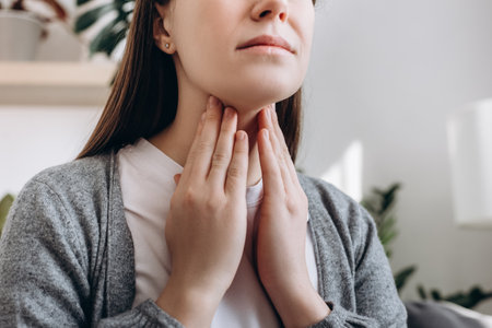 Selective focus of unhealthy sad young caucasian woman hold hands over sore throat feeling discomfort. Painful neck and frowning, thyroid disorders, suffering sore throat, tonsils inflammation conceptの写真素材
