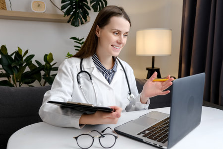 telehealth concept. Happy attentive general practitioner in uniform and stethoscope using laptop, giving online help, medical support, consultation, talking to patients, making video conference callの写真素材