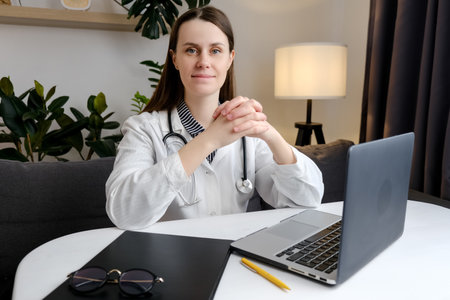 Portrait of smiling young woman nurse sitting at desk in hospital or private clinic. Happy positive caucasian female doctor in white medical uniform and stethoscope at workplace. healthcare conceptの写真素材