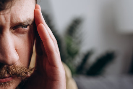 Cropped portrait of sad young caucasian man suffering from migraine while staying alone at apartment. Unhappy sad male massaging temples, mental stress, panic attack touching aching sore headの写真素材
