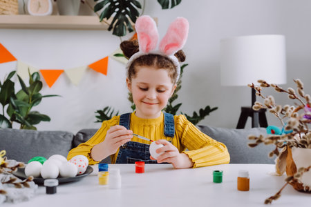 Adorable happy little girl child playing, drawing and decorating egg. Beautiful smiling small kid paint and decorate eggs for traditional spring holiday at home. easter family traditions conceptの写真素材
