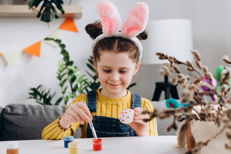 Close up portrait of pretty little girl child playing, drawing and decorating egg. Adorable smiling kid paint and decorate eggs for traditional spring holiday at home. easter family traditions conceptの写真素材