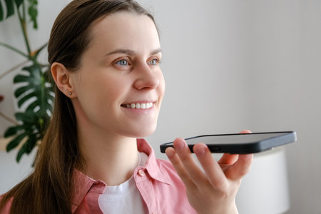 Easy mobile ai technology concept. Close up of smiling young woman holding phone speak activate virtual digital voice assistant on smartphone, happy girl ask internet assistance service make callの写真素材