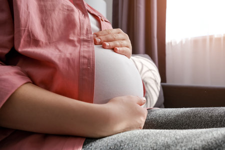 Close up of loving young pregnant woman sitting on sofa stroking big belly, expressing love and care to unborn baby, expecting childbirth, feeling tenderness, resting alone. happy maternity conceptの写真素材