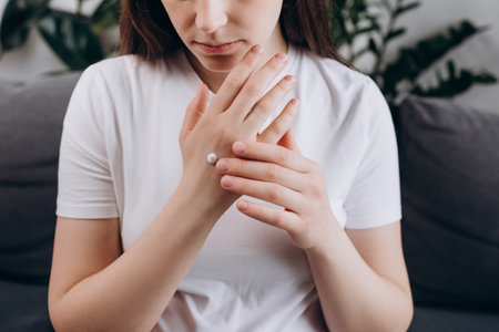 Close up of young caucasian woman 20s old years rubbing moisturizing cream on hand skin, resting alone on cozy sofa in living room at home. Pregnancy, motherhood and beauty. Hand care conceptの写真素材