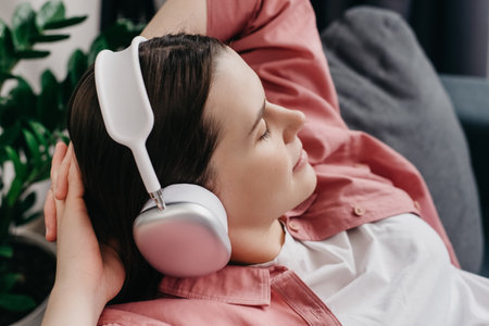 Close up of serene satisfied young caucasian woman lying on cozy couch wearing wireless headphones enjoy listen modern music audio book with eyes closed meditate relax feel no stress chill at homeの写真素材