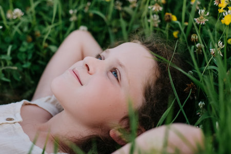 Portrait of relaxed smiling charming little girl kid lying on fresh green grass in park at summer day. Carefree pretty preteen child lie on field and enjoying weekend. nature and childhood conceptの写真素材