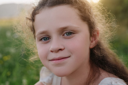 Pretty happy kid poses funny and smiling enjoying outdoors during sunset. Close up portrait of charming little girl looking at camera with laughing and giggling expression. Childhood and leisure timeの写真素材
