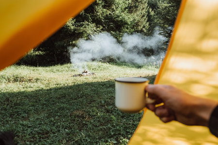 Selective focus of unknown young caucasian man holding hot coffee from hiking travelling mug on...