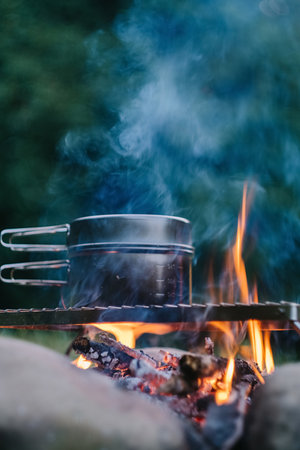 Close up of boiling water in black pot over campfire on background green at warm evening time. Bonfire cooking in summer season. Concept of adventure, travel and hiking. fast dinner campingの写真素材