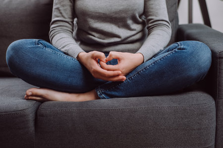Unrecognizable young caucasian woman folded hands on knees together, sitting on sofa, unhappy female...
