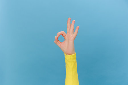Close up of female hand makes shape that means OK, posing isolated over blue color background wall in studio with copy space for promotion content or design. Communicating meanings using body languageの写真素材
