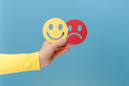 Close up of female hand holding happy and angry face paper, isolated on blue studio background. Feedback rating, emotional intelligence, control, mental health assessment, bipolar concept disorderの写真素材