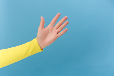 Closeup of woman hand waving hand, showing palm, making hello or good bey gesture, greeting or acclaiming concept, posing isolated over plain blue color background wall in studio with copy spaceの写真素材