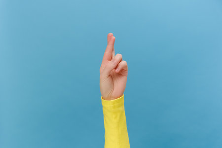 Close up of female hands praying with crossed fingers hopes for a miracle good outcome, isolated over blue studio background with copy space. Body language concept. Advertising area, workspace mock upの写真素材