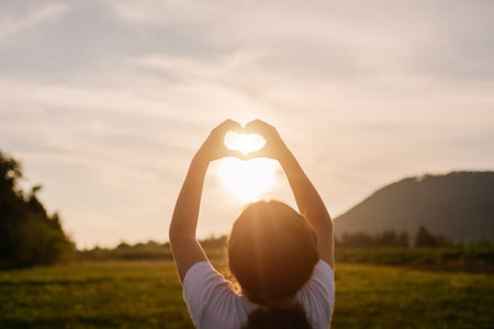 Cute little girl child making heart with hands during warm sunset or sunrise at summer day. Sunbeams Sunlight. Happy Valentines day, Mothers Day, love nature or life happiness conceptの写真素材
