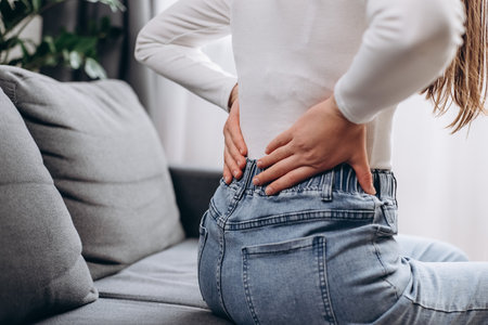 Close up of suffer young woman painful with back pain, back ache sitting on sofa at home holding massaging rubbing shoulder hurt, sore. Pain body muscles stiff. Health care and medical conceptの写真素材