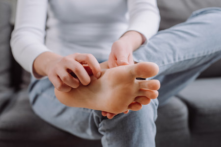 Close up of woman doing self foot massage for pain relief after fatigue, long walking, working, standing, flat feet or injury, sitting on sofa. Suffering from hurt of arch, ball, heel or toe treatmentの写真素材